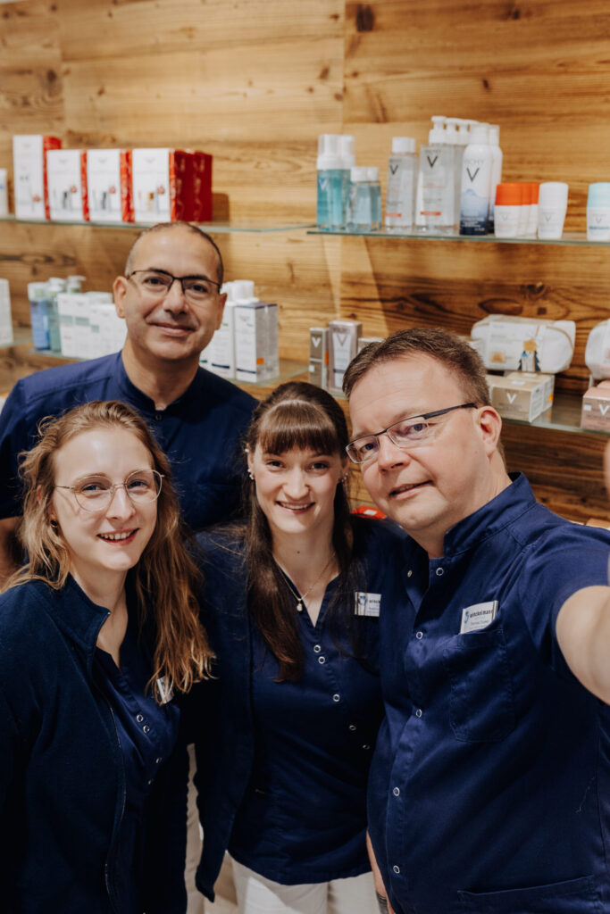 Vier lächelnde Mitarbeitende machen ein Selfie vor einem Regal mit Pflegeprodukten.