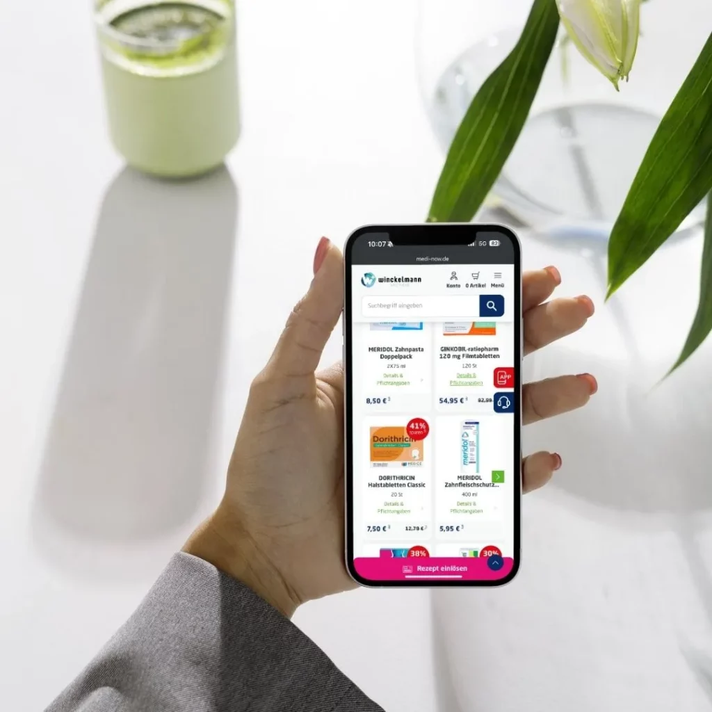 Eine Hand hält ein Smartphone mit dem Onlineshop der Winckelmann Apotheke, der reduzierte Produkte und die Schaltfläche „Rezept einlösen“ zeigt.