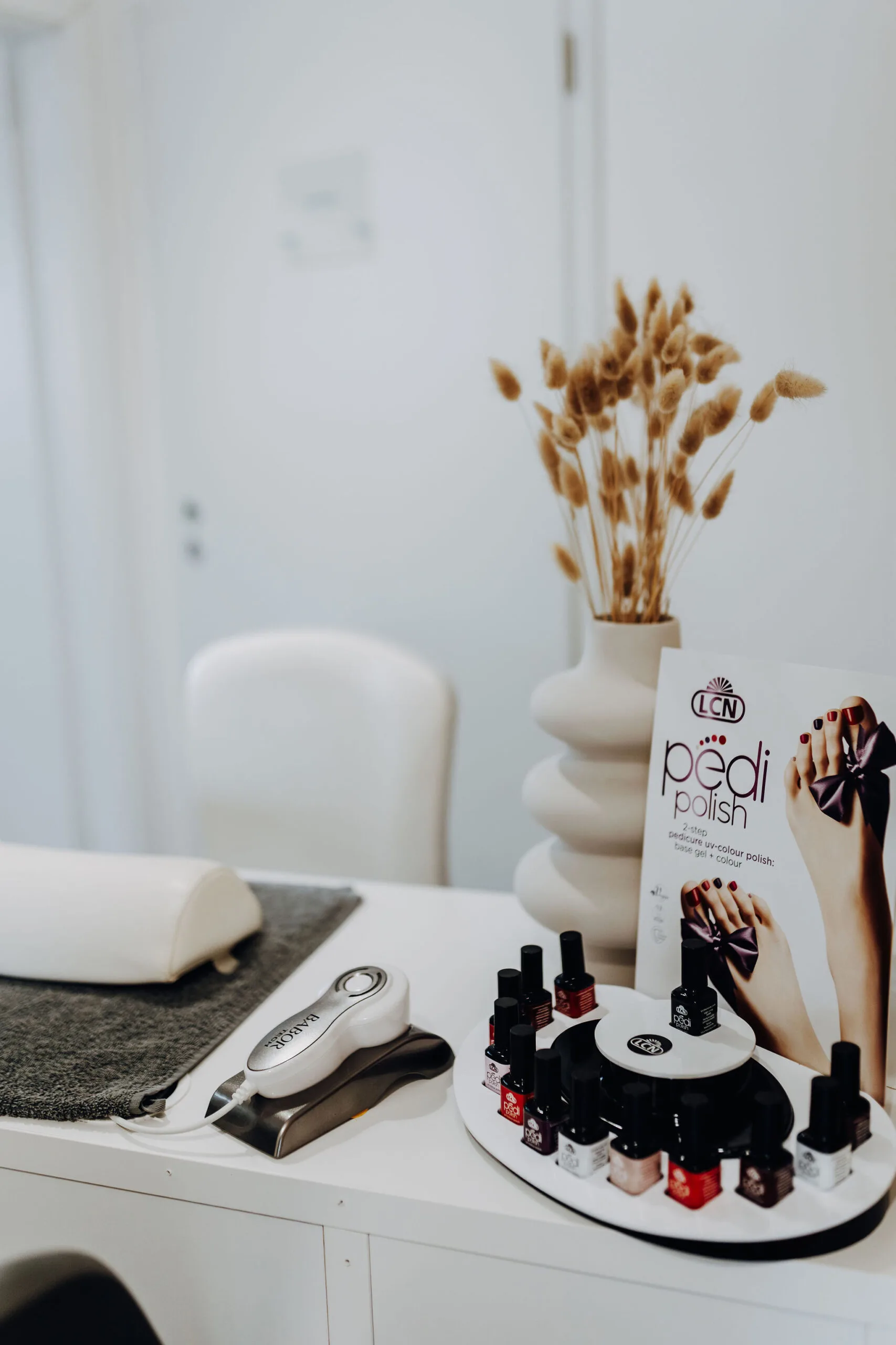 Nagellackfläschchen und ein Pflegegerät stehen auf einem Tisch im Kosmetik- und Fußpflegebereich.