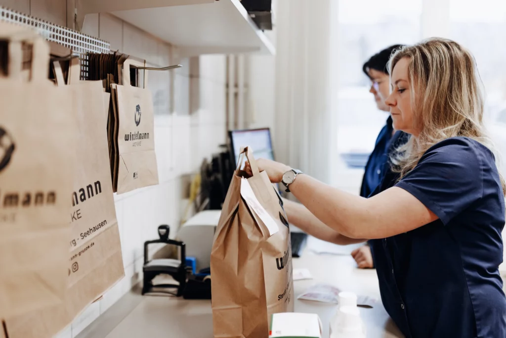 Zwei Mitarbeiterinnen verpacken Kundenbestellungen in Papiertüten mit dem Winckelmann-Logo.